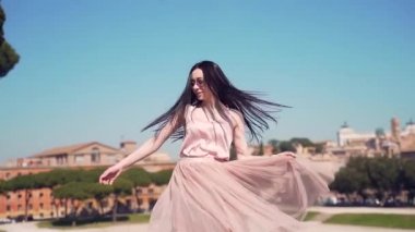 Çekici seksi ve mutlu esmer kız portresi kameraya poz veriyor, gülümsüyor ve şehir mimarisinin arka planındaki kaldırımlı meydanda dönüyor. Roma, İtalya. Elbise içinde gülümseyen turist.