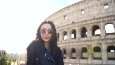 Colosseum 'un arka planında genç bir kızın portresi. Güneş gözlüklü çekici kadın kameraya poz veriyor. İtalya, Roma amfi tiyatrosunun arka planında kadın turist.