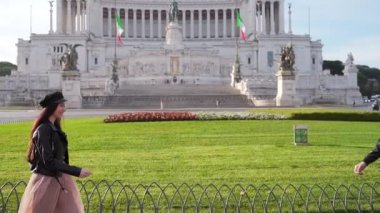 Vittoriano, Piazza Venezia 'nın arka planında genç turistler buluşuyor. Kız adama yaklaşıyor, el ele tutuşuyor, randevuda sarılıyor. Roma İtalya. Kare. Siyah elbiseli hippiler.