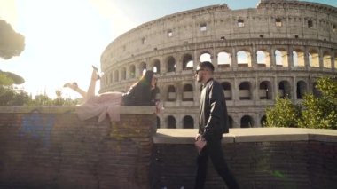 Colosseum 'un arka planında genç ve şık bir çift turist. Roma, İtalya. Adam kıza sarılıp el ele tutuşarak yaklaşıyor. Havalı hippiler siyah kıyafetler ve elbiseler içinde mutludur..