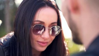 yakın plan portre, esmer kız gülümsüyor ve adama bakıyor, adam güneş gözlüklerine yansıyor. Dışarıda mutlu bir gülümseme, yaz ya da sonbahar. Şık, mutlu, çekici bir kadın..