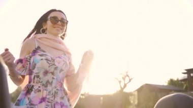 Üstü açık bir arabanın arka koltuğunda oturan, mutlu bir şekilde gülümseyen ve yolda araba süren genç ve çekici bir kadın. Rüzgar saçlarını savuruyor. Kadın arabanın üstünden gülüyor. Yavaş çekim