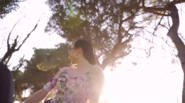 Üstü açık bir arabanın arka koltuğunda oturan, mutlu bir şekilde gülümseyen ve yolda araba süren genç ve çekici bir kadın. Rüzgar saçlarını savuruyor. Kadın arabanın üstünden gülüyor. Yavaş çekim