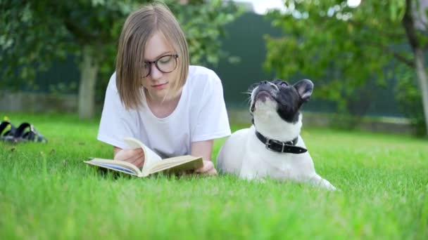 Веселый Студент Читает Книгу Сидя Парке Затем Гладит Очаровательного Щенка — стоковое видео