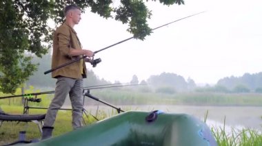 Balıkçı elinde dönen ya da balık tutan bir çubukla gölün kenarında duruyor. Adam makarayı tutarken yakalıyor. Şişme bot, sandalye. Sabah sisi ağacı. Ekipman balığı takımları. Kamp ve hobi. Bir hipster portresi. 