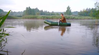 Genç, şık hippi balıkçı sazlıklar arasında bir gölde ya da nehirde yelken açar. Genç bir adam şişme bir teknede kürek çekiyor. Doğada rahatlar. Suyun kenarında kamp yapmak. Rekreasyon