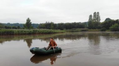 Genç, şık hippi balıkçı sazlıklar arasında bir gölde ya da nehirde yelken açar. Genç bir adam şişme bir teknede kürek çekiyor. Doğada rahatlar. Suyun kenarında kamp yapmak. Rekreasyon
