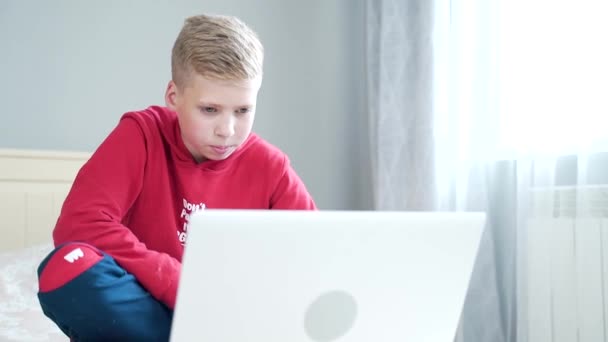 可爱的英俊和快乐的男孩 青少年 坐在或躺在房间的床上看视频笑 学习课 男生看笔记本电脑 这个家伙浏览了一下互联网 写了些什么 — 图库视频影像