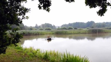 Genç, şık hippi balıkçı sazlıklar arasında bir gölde ya da nehirde yelken açar. Genç bir adam şişme bir teknede kürek çekiyor. Doğada rahatlar. Suyun kenarında kamp yapmak. Rekreasyon
