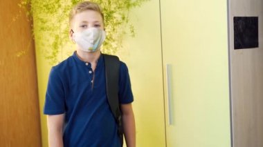 Okul çocuğu elinde bir dosya ve koruyucu tıbbi maskeli bir odada sırt çantasıyla duruyor. Genç çocuk bir odada ya da okulda duruyor ve kameraya bakıyor.