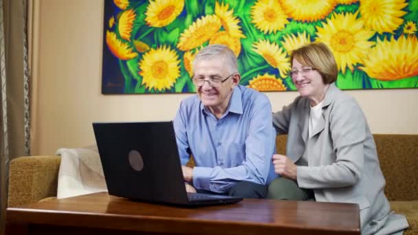 可爱迷人的祖父母在黑色笔记本电脑上给家人打电话 挥挥手 上了年纪的夫妻坐在客厅里笑着 在家里用孤立的电脑 — 图库视频影像