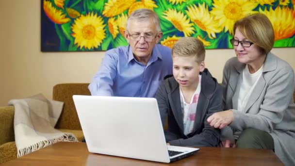 兴奋的祖父母坐在客厅里 手拉着电脑与孙子一起学习一些东西 在检疫期间 祖父母和孙子孙女在客厅里使用笔记本电脑 — 图库视频影像