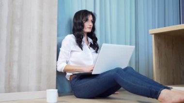 Kız öğrenci odada yerde oturuyor, dizüstü bilgisayar telefonu ve belgelerle çalışıyor. Evde uzaktan öğrenme. Genç bayan üniversite öğrencisi internetten öğrenim görüyor. Sınavları geçer