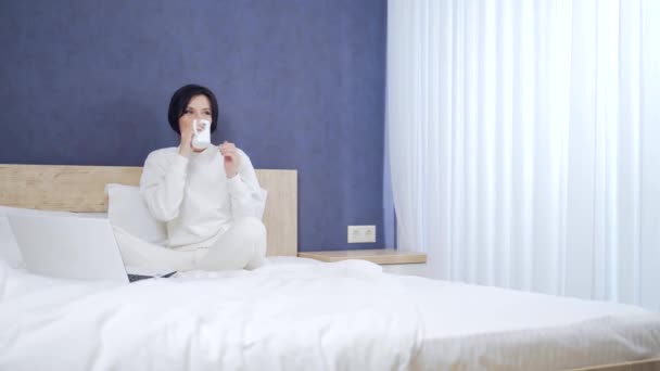 young sick business woman manager working at home in bed during illness. Female in white pajamas or a sports suit works on the sofa in the morning with a laptop and documents. businesswoman in bedroom