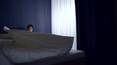 Pijamalı genç esmer kadın sabah uyanır ve yatak odasında yataktan kalkar ve pencerenin kenarına uzanır. Siluet kadın, bir evde dinleniyor. Karanlık bir odada.