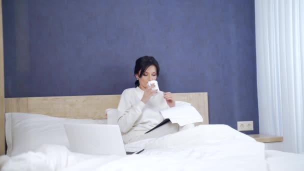 生病时在家里工作的年轻生病的女经理 穿着白色睡衣或运动服的女人们带着笔记本电脑和文件在沙发上工作 卧室里的女商人 — 图库视频影像