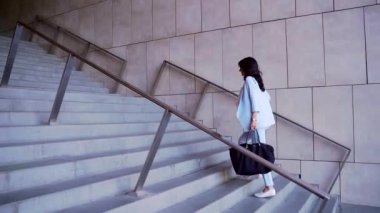 Güzel çekici bir iş kadını alelacele saate bakar ve ofis binasına doğru merdivenlerden çıkar. İşe dizüstü bilgisayarla koşan esmer ve büyük siyah çantalı, mavi takım elbiseli..