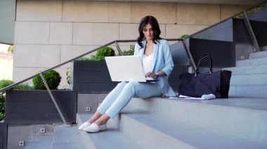 Resmi olarak genç iş kadını dışarıda dizüstü bilgisayarla oturuyor. İş merkezinin merdivenlerinde çalışan serbest çalışan bir iş kadını. Sokaktaki ofis. Gözlüklü ve takım elbiseli esmer.