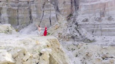 Çıplak gövdeli yakışıklı bir adam ve uzun kırmızı elbiseli güzel bir kadın kayalık dağların ortasında dans ediyorlar. Dans sanatı ve doğayla bağlantı kavramı. hava görünümü
