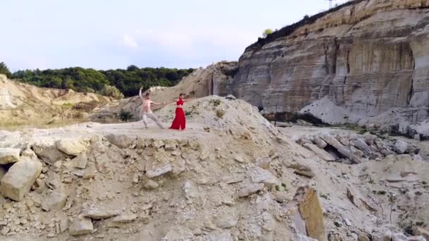 岩の多い山の真ん中で一緒に踊る長い赤いドレスで裸の胴と美しい女性とハンサムな男 ダンスアートの概念と自然とのつながり 空中の眺め — ストック動画
