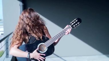 ... siyah şık elbiseli ve güneş gözlüklü, modaya uygun, genç bir bayan gitarist, yürüyen ve otoparkta kameraya bakan genç ve şık bir bayan. Şehir arkaplanı