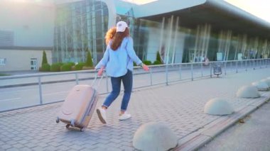 Genç şık kız hippi turist bir bavul işletiyor ve şehir arka planında havaalanına ya da otobüs durağına gitmek için geç kalıyor. Sokakta aceleyle koşan bir öğrenci.