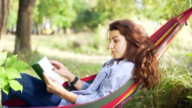 Genç Yetişkin Bir Kızın Hamakta Yatıp Parkta Doğa Üzerine Bir Kitap Okurken Portresi 'ni Kapatın. Pretty Woman, elinde bir kitapla dinleniyor ve rahatlıyor. Bir hippi öğrenci dışarıda öğreniyor..