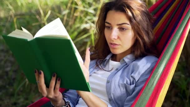 ハンモックに横たわって自然公園で本を読んでいる若い大人の女の子の肖像画を閉じます 美しい女性の休息と手に本でリラックス 学生のヒップスターは屋外で学ぶ — ストック動画