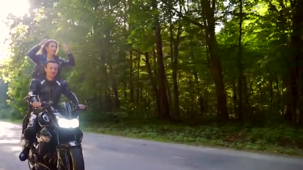 Jovem casal monta uma motocicleta em uma estrada florestal — Vídeo de Stock