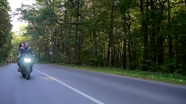 Молодая пара едет на мотоцикле по лесной дороге — стоковое видео