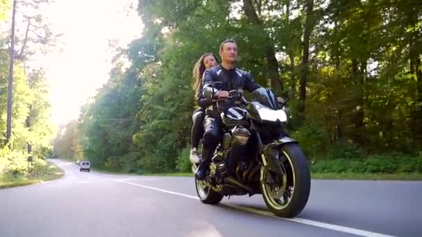 Pareja joven monta una motocicleta en un camino forestal — Vídeos de Stock
