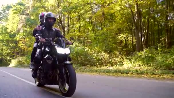 Pareja joven monta una motocicleta en un camino forestal — Vídeos de Stock