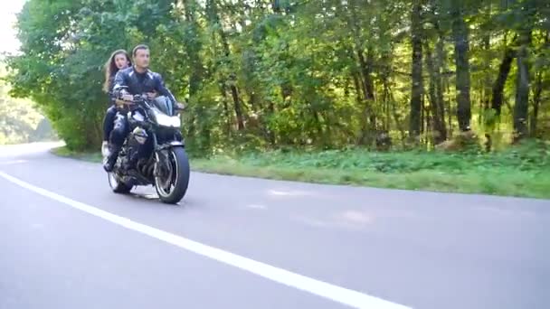 Jovem casal monta uma motocicleta em uma estrada florestal — Vídeo de Stock