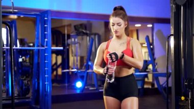Spor kulübünde şişeden su içen çekici genç kadın vücut geliştiricinin portresi. Güçlü bir atletik kız spor salonunda susuzluğunu giderir. Egzersizden sonra güzel seksi spor eğitmeni