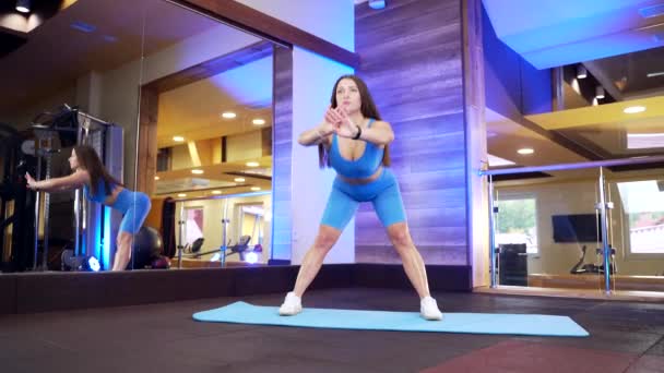 mladá sexy fitness žena v modrém sportovním oblečení dělá cvičení s zahřívání a protahování na podložce před zrcadlem. sportovní dívka, sportovec se zahřívá před tréninkem v tělocvičně nebo klubu