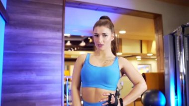 Spor giyim bölümünde güçlü kaslı seksi bir antrenör kadın portresi. Egzersiz makinelerinin arka planında kameraya poz veren kendinden emin genç bir sporcu ya da vücut geliştirici kız.