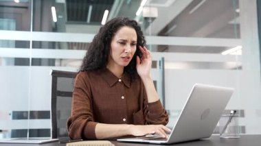 İş yerinde çalışırken dizüstü bilgisayarla uğraşırken baş ağrısı çeken yorgun bir iş kadını. Üzgün, yorgun genç bir kadın acı hissediyor ve elleriyle şakaklarına masaj yapıyor.