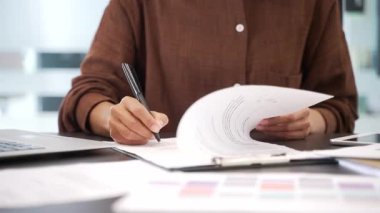 İş yerindeki bir masada kadın el imzalı evrakları kapatıyoruz. Kendine güvenen bir iş kadını yöneticisi dosyasına belgelerle bakar ve sözleşmeyi bir kalemle imzalar.