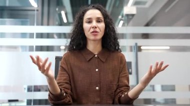 Webcam görüntüsü. Kendine güveni tam bir iş kadını video konferansında modern iş ofisinde oturan kameraya bakıyor. Kadın antrenör veya öğretmen çevrimiçi eğitim, danışma, kurs veya webinar