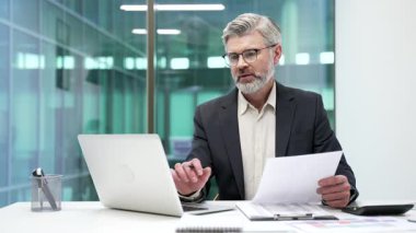 İş yerindeki bir masada otururken bir dizüstü bilgisayardaki verileri inceleyen resmi bir takım elbiseyle meşgul bir işadamı. Olgun ciddi finansör mali raporla ilgilenir