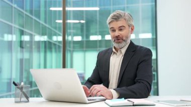 Memnun iş adamı iş yerinde otururken dizüstü bilgisayarından harika haberler aldı. Resmi takım elbiseli yetişkin bir girişimci bilgisayardan olumlu bir mesaj okuyor.