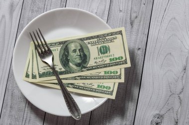 Hafif ahşap arka plan üzerinde bir çatal ile bir tabak içinde yüz dolar faturaları yalan