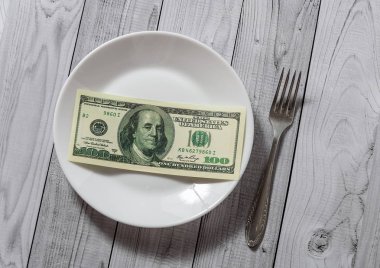 Hafif ahşap arka plan üzerinde bir çatal ile bir tabak içinde yüz dolar faturaları yalan