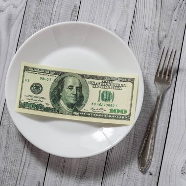 Hafif ahşap arka plan üzerinde bir çatal ile bir tabak içinde yüz dolar faturaları yalan