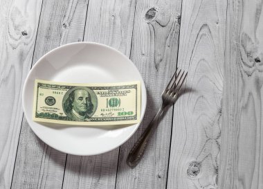 Hafif ahşap arka plan üzerinde bir çatal ile bir tabak içinde yüz dolar faturaları yalan