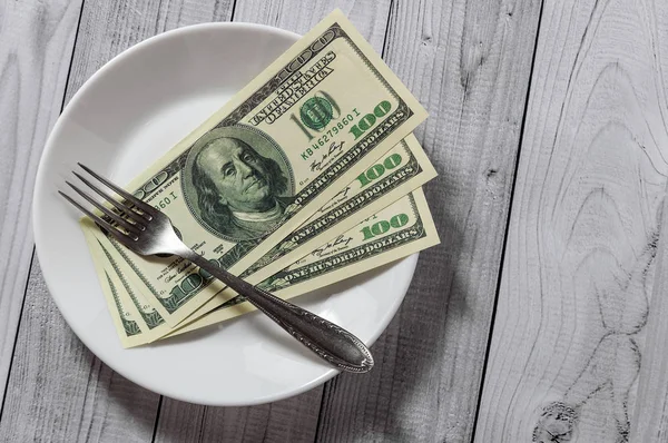 Hafif ahşap arka plan üzerinde bir çatal ile bir tabak içinde yüz dolar faturaları yalan