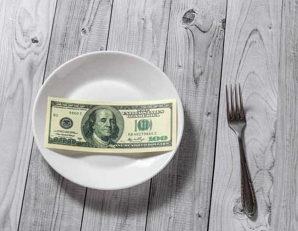 Hafif ahşap arka plan üzerinde bir çatal ile bir tabak içinde yüz dolar faturaları yalan