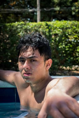 Havuzda kameraya bakan genç, ıslak bir adam. 