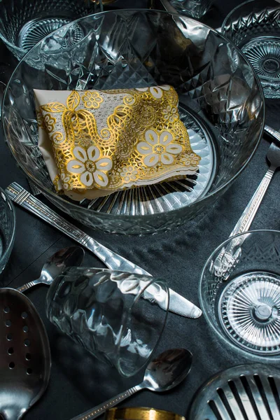 Gümüş çatal bıçak seti, cam tabaklar, cam kaplar ve siyah bir masa üzerindeki bardaklar. 
