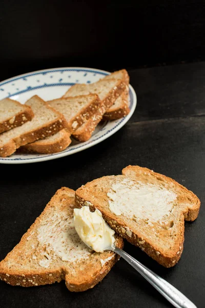 一些全麦面包和黄油在盘子里的木制黑桌上 — 图库照片
